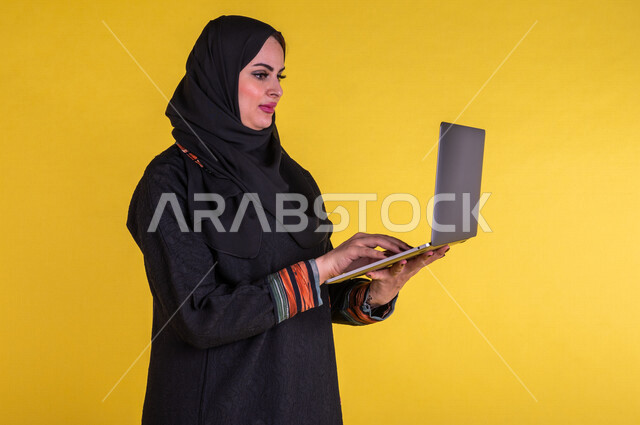 بورتريه لسيدة عربية خليجية سعودية تستخدم الحاسوب المحمول لانجاز الاعمال عن بعد ، اجراء مكالمات الفيديو ، مشاهدة البرامج والافلام ،  التسويق الالكتروني ، تصفح الانترنت ،  خلفية صفراء