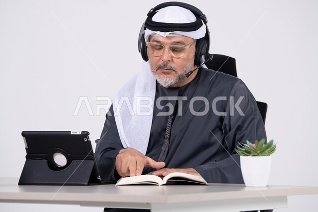رجل إماراتي يرتدي سماعات الرأس ويقرأ كتاباً في الاستوديو