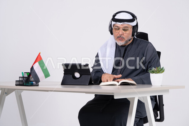 رجل إماراتي يرتدي سماعة رأس في مكتب مع علم الإمارات