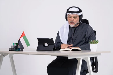 رجل إماراتي يرتدي سماعة رأس في مكتب مع علم الإمارات رجل إماراتي يرتدي سماعة رأس في مكتب مع علم الإمارات