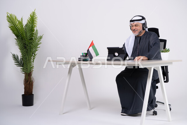 رجل أعمال إماراتي يستخدم الجهاز اللوحي والسماعة بالمكتب
