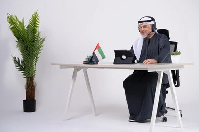 رجل أعمال إماراتي يستخدم الجهاز اللوحي والسماعة بالمكتب