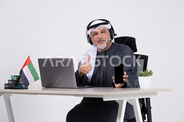 Emirati Businessman with Headset Holding Smartphone at Desk
