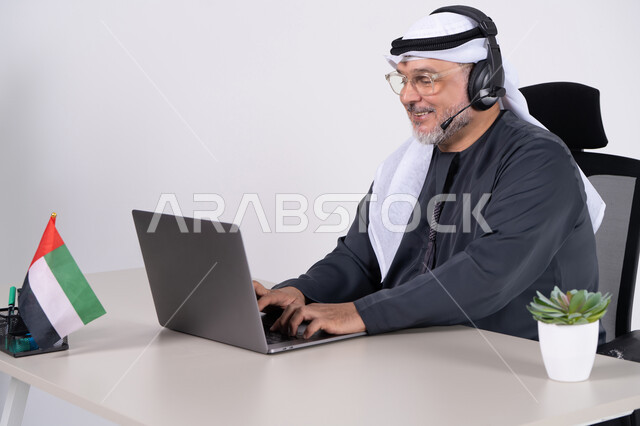 Emirati Man Working on Laptop with Headset in Office