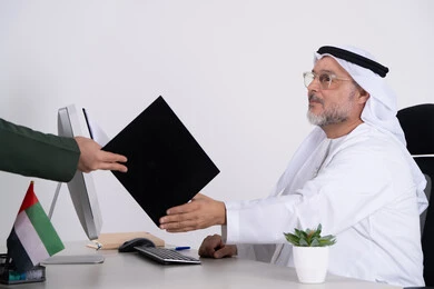 رجل أعمال إماراتي يستلم ملفاً في مكتب أبيض