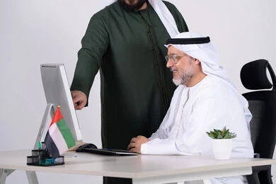 رجال أعمال إماراتيون يعملون على الكمبيوتر في المكتب