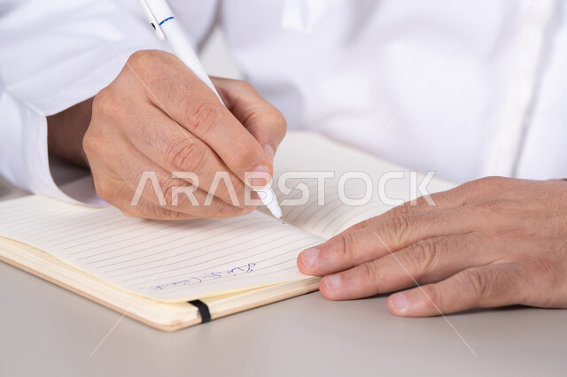 رجل إماراتي يكتب في دفتر ملاحظات لقطة مقربة