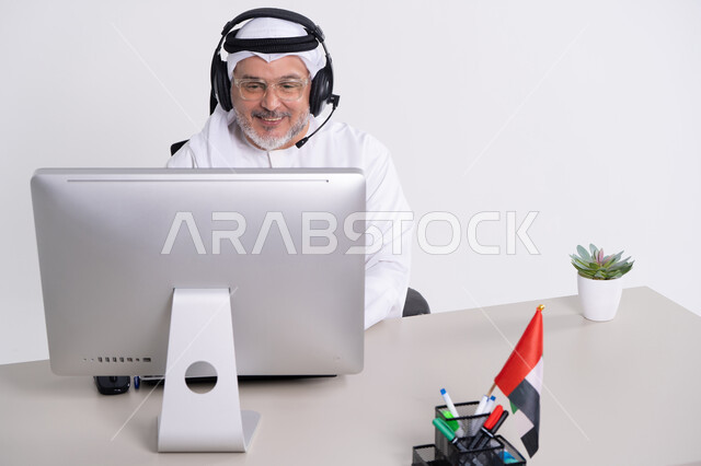 رجل أعمال إماراتي يرتدي سماعة أمام الكمبيوتر