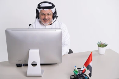 رجل أعمال إماراتي يرتدي سماعة أمام الكمبيوتر