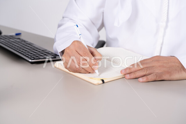 رجل سعودي يرتدي الثوب يكتب في مفكرة على المكتب