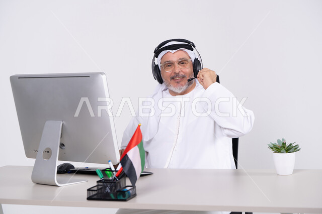 رجل إماراتي يرتدي سماعة رأس ويعمل على الكمبيوتر