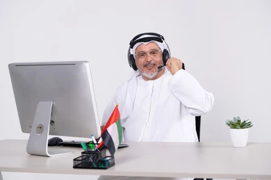 رجل إماراتي يرتدي سماعة رأس ويعمل على الكمبيوتر