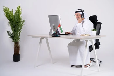 رجل إماراتي يعمل على الكمبيوتر في مكتب أبيض