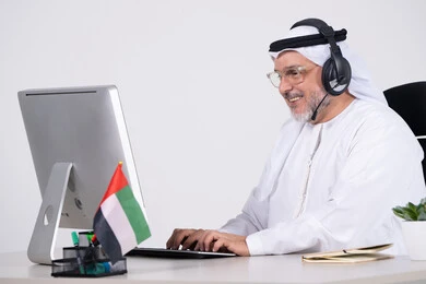 رجل أعمال إماراتي يعمل على الكمبيوتر بسماعة رأس