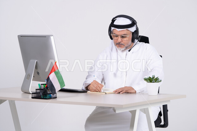 رجل إماراتي في المكتب مع سماعة رأس وجهاز كمبيوتر