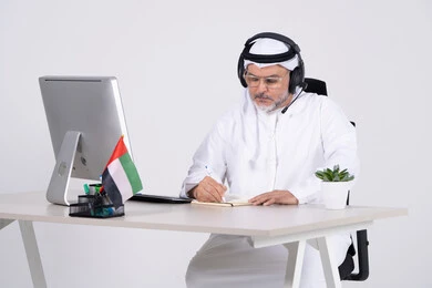 رجل إماراتي في المكتب مع سماعة رأس وجهاز كمبيوتر