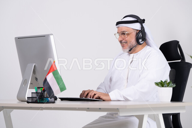رجل إماراتي يعمل على الكمبيوتر بسماعة رأس