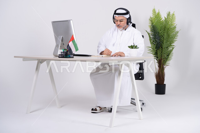رجل أعمال إماراتي مع سماعة رأس يعمل على المكتب