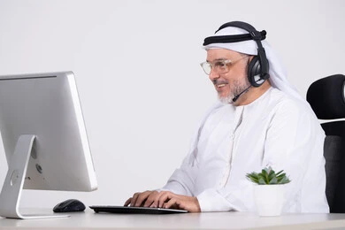 رجل أعمال إماراتي يعمل على الحاسوب بسماعة رأس