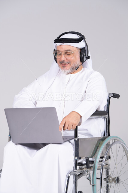 رجل إماراتي على كرسي متحرك يستخدم اللابتوب والسماعات