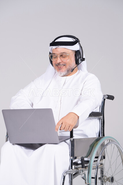 رجل إماراتي على كرسي متحرك يستخدم لابتوب وسماعة