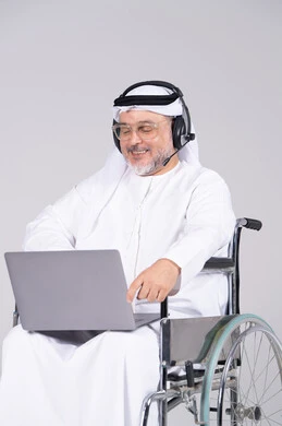 رجل إماراتي على كرسي متحرك يستخدم لابتوب وسماعة