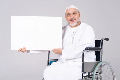 رجل إماراتي مسن على كرسي متحرك يحمل لوحة بيضاء