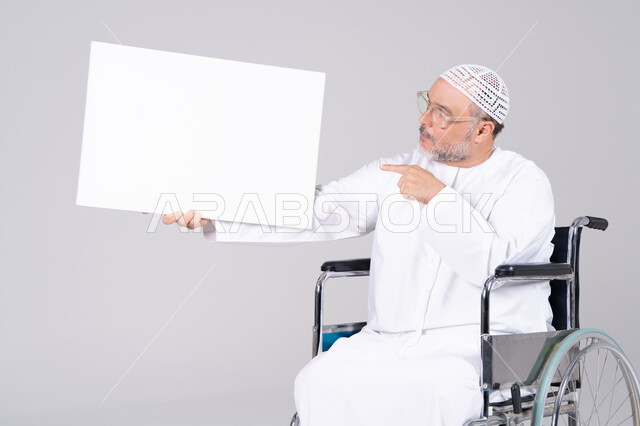 رجل إماراتي مسن على كرسي متحرك يحمل لوحة فارغة
