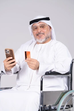رجل إماراتي مسن على كرسي متحرك يحمل بطاقة ائتمان