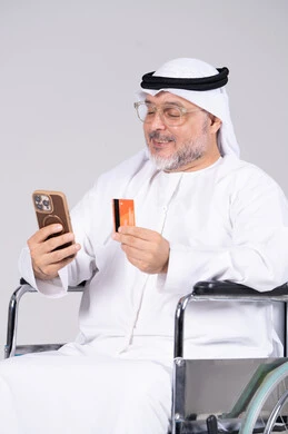 رجل إماراتي مسن على كرسي متحرك يستخدم الجوال والبطاقة