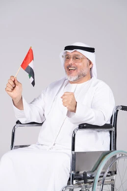 رجل إماراتي مسن على كرسي متحرك يحمل علم الإمارات