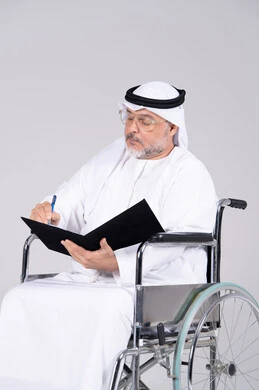 رجل إماراتي على كرسي متحرك يكتب في ملف خلفية بيضاء