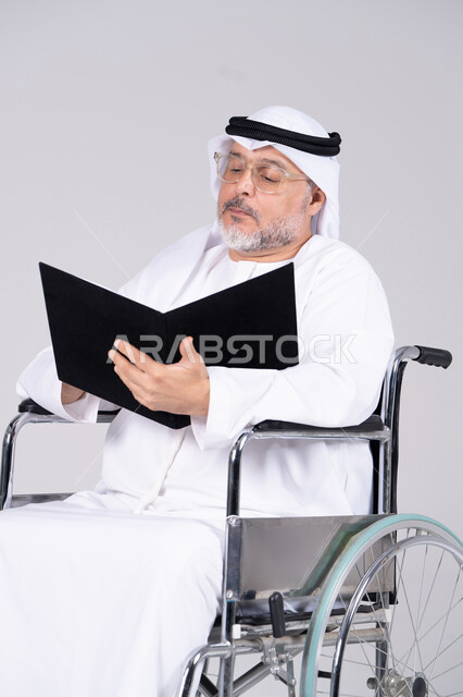 رجل إماراتي مسن على كرسي متحرك يقرأ مجلد