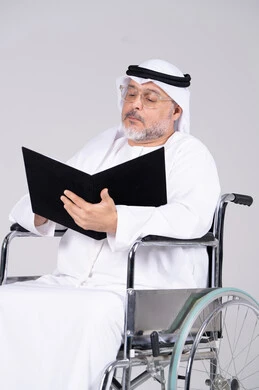 رجل إماراتي مسن على كرسي متحرك يقرأ مجلد