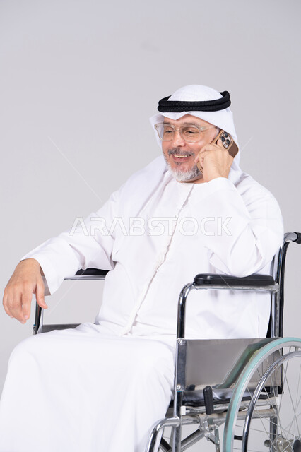 رجل إماراتي مسن على كرسي متحرك يستخدم الهاتف