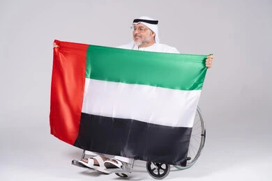 رجل إماراتي على كرسي متحرك يحمل علم الإمارات