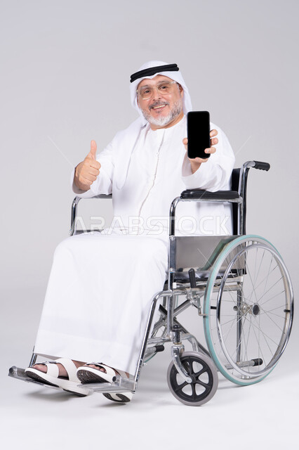 رجل إماراتي على كرسي متحرك يحمل هاتفاً ذكياً لقطة كاملة