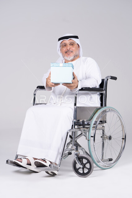 رجل إماراتي مسن على كرسي متحرك يحمل هدية