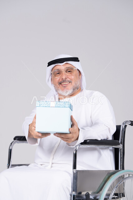 رجل إماراتي مسن على كرسي متحرك يحمل هدية