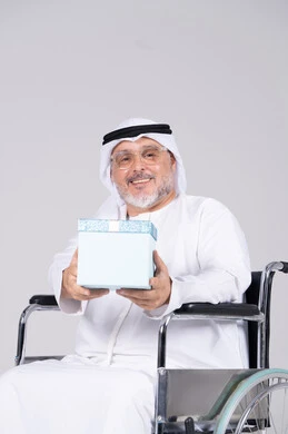 رجل إماراتي مسن على كرسي متحرك يحمل هدية