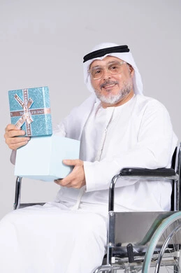 رجل إماراتي مسن على كرسي متحرك يحمل هدية