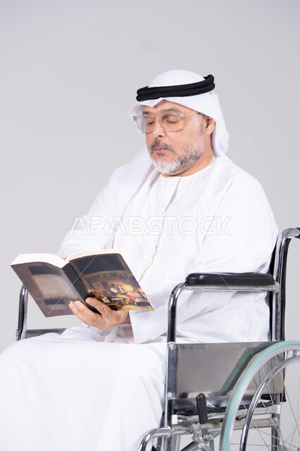 رجل إماراتي مسن على كرسي متحرك يقرأ كتاباً