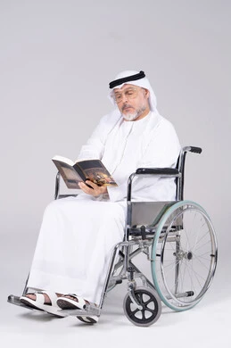 رجل إماراتي مسن على كرسي متحرك يقرأ كتاب
