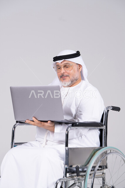 رجل إماراتي مسن على كرسي متحرك يستخدم اللابتوب
