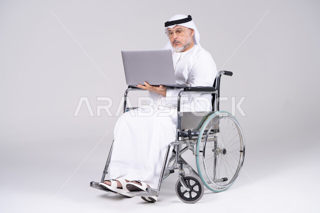 رجل إماراتي مسن على كرسي متحرك يستخدم لابتوب خلفية بيضاء