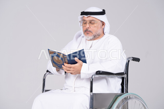 رجل إماراتي مسن على كرسي متحرك يقرأ القرآن