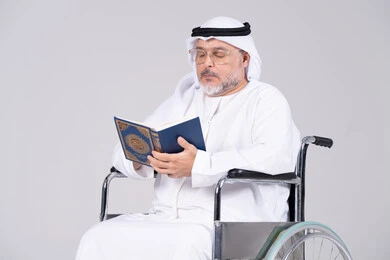 Emirati Senior Man in Wheelchair Reading Quran