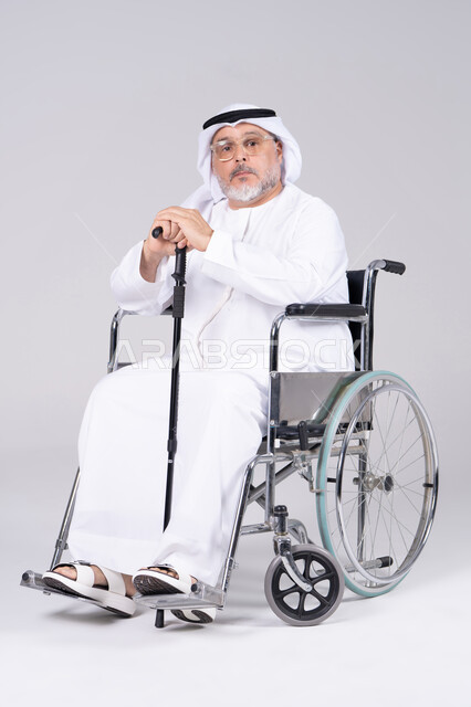 رجل إماراتي مسن على كرسي متحرك بخلفية رمادية