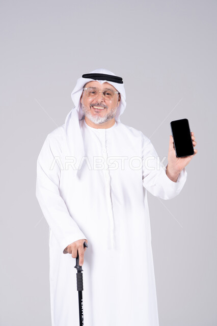 رجل إماراتي مسن يحمل هاتفاً ذكياً بشاشة فارغة