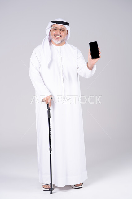 رجل إماراتي مسن يحمل هاتف ذكي مع عصا مشي
